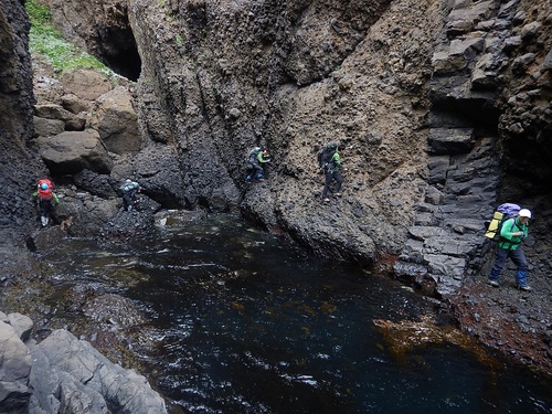 切り立った岩壁をトラバースする職員。足下には深い溝があり、海水で充ち満ちている。（2018年6月撮影）